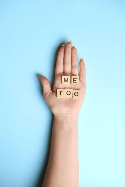 Phrase Me Too made of wooden letters in hand on blue background, top view. Stop sexual assault. Space left for text, copy