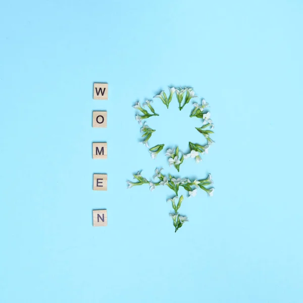 Top view women spelled in wooden blocks on blue background with woman gender sign made of flowers. Love, 8 march background. Gift, greeting, compliment concept. Copy space. place for text. — Stockfoto