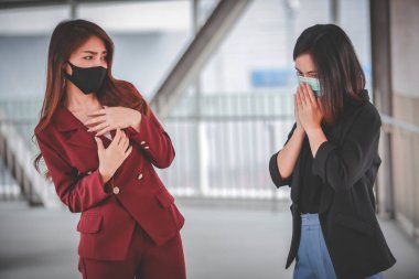 Kadın endişeli ve korku dolu. Dışarıdaki medikal maskeli bayan arkadaş öksürüyor. Mesafeyi koru Corona virüsünü durdur.