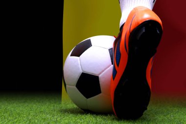 Futbol oyuncusunun bacakları ve ayakları kapalı, yeşil çimlerde yürüyor, Belçika bayrağının arka planında maç yapmaya hazır..