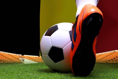 Futbol oyuncusunun bacakları ve ayakları kapalı, yeşil çimlerde yürüyor, Belçika bayrağının arka planında maç yapmaya hazır..