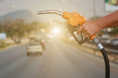 Arabalarda yakıt hortumu tutan eller ve caddelerdeki kara taşımacılığı arka planda..