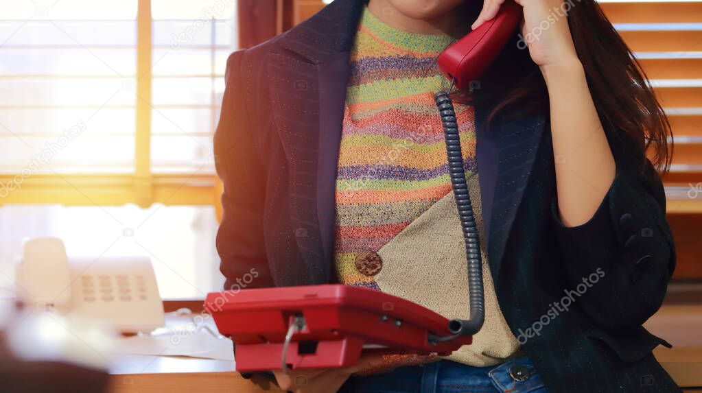 Portrait of  pretty lovely bright young business woman on workplace standing holding a red office telephone and with and other supplies.