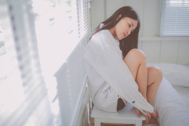 Pencerenin yanındaki sandalyede oturan üzgün Asyalı kadının yakın görüntüsü.