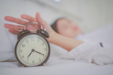 Sabah vakti klasik çalar saate odaklan ve yatak odasındaki beyaz yatakta uyuyan genç kadına odaklan..