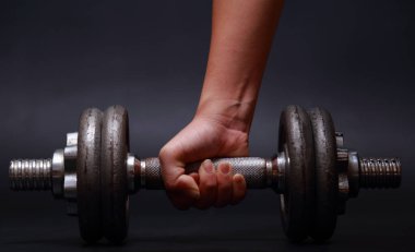 Koyu arkaplanda dambılı kolları olan çekici atletik bir kadın..