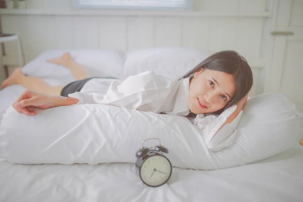 Sleepy asian woman in bed with alarm clock near.