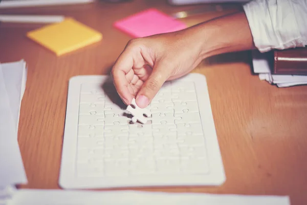 Work planning meeting hand holding Jigsaw puzzle on a catching paper business documents, the office table and have orange light. Concept Working as a team has been successful.