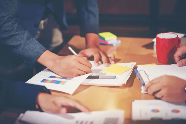 Work planning meeting hand holding pen and catching paper business documents, analyzing the market and weighing on the size of future profits on the office table and have orange light.