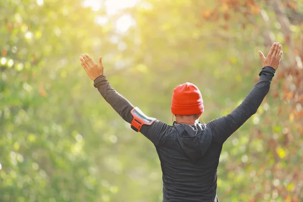 The man warms up muscles before jogging in forest with sunlight path in late summer or fall. fitness healthy lifestyle concept.