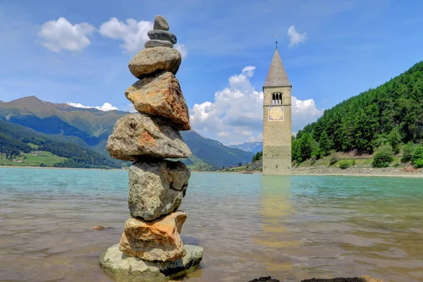 Rock Cairn perto da torre da igreja subaquática em Reschensee Lake, Ital — Fotografia de Stock