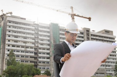 İnşaat alanının planlarını ve planlarını elinde tutan mühendis.