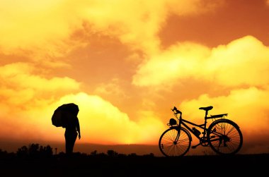 Gün batımında güzel bulutlar ve ufuklarla bisiklet ve şemsiyeyle tanınmayan bir kızın silueti.  