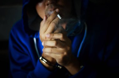 Duvarın yanında sigara içen, stresten sigara içen mavi kapüşonlu adamla siyah bir fotoğraf.