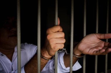 Demir parmaklıklar ve beyaz gömlekli bir adamın elleri nezarethanede. 