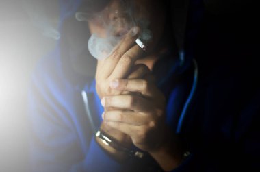 Duvarın yanında sigara içen, stresten sigara içen mavi kapüşonlu adamla siyah bir fotoğraf.