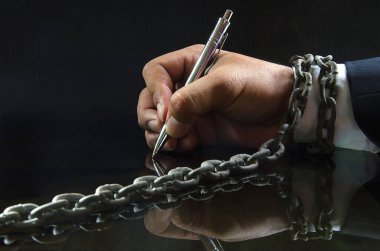 Eski çelik bir zincire sarılmış, siyah arka planda parlak bir yüzeye kalemle yazı yazan takım elbiseli bir adamın eli.