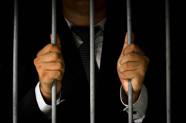 Close-up Of Businessman Hands Holding Metal Bars In Jail with dar