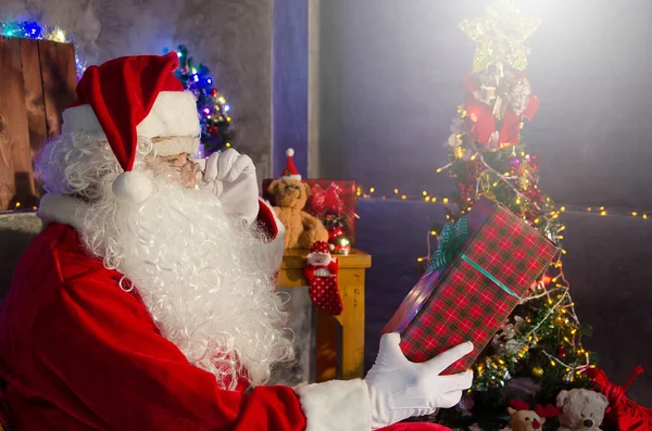 Kerstman Zit Stoel Houdt Een Geschenk Met Een Versierde Kerstboom — Stockfoto