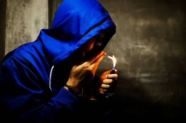 与身穿蓝色帽衫的男子在舞台灯光下在墙边吸烟的深色照片 — 图库照片