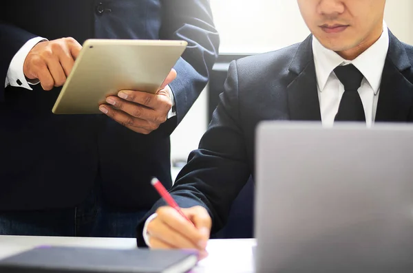 Bir iş akışı, elinde tablet tutan ayakta duran bir adamın görüntüsü ve dizüstü bilgisayarın yanında oturan ve bir şeyler yazan başka bir adama bir şeyler göstermek.