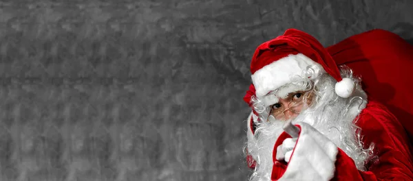 圣诞老人在灰色的背景下把大袋子扛在肩上 — 图库照片