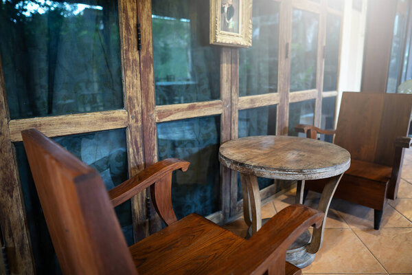part of the cafe with a view of a wooden table and two wooden chairs standing under an old large wooden window and a small painting above them 