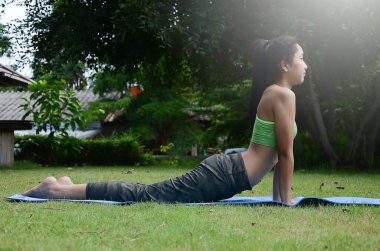 Genç bir kadın parkta yoga yapıyor, geriniyor.