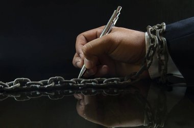 Kalem tutan bir iş adamının elleri zincirli. Koyu bir sırta karşı