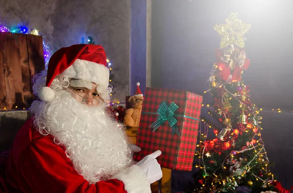 Santa Claus Sedí Židli Drží Nějaký Dárek Zdobeným Vánočním Stromečkem — Stock fotografie