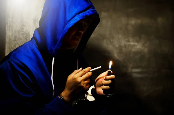 与身穿蓝色帽衫的男子在舞台灯光下在墙边吸烟的深色照片 — 图库照片