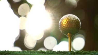 Yeşil çimlerin üzerinde güneş ışığıyla aydınlatılmış altın golf topunun yakın çekim görüntüleri