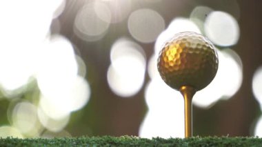Yeşil çimlerin üzerinde güneş ışığıyla aydınlatılmış altın golf topunun yakın çekim görüntüleri