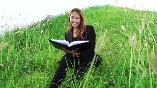 Yeşil Çimlerin Üzerinde Oturan Asyalı Kadın Kitap Okuyor — Stok video