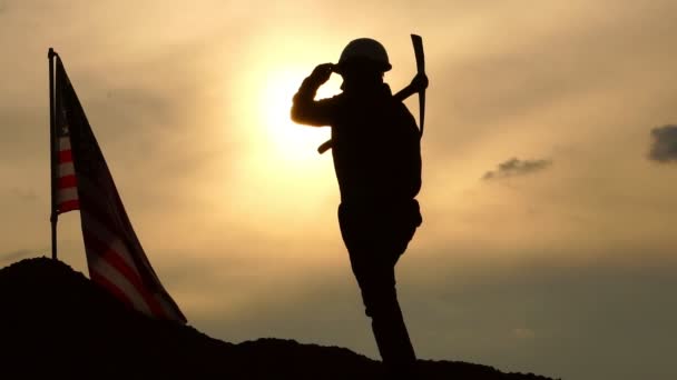 在多云的天空背景下 拿着镐在山上挥舞着美国国旗的工人 — 图库视频影像
