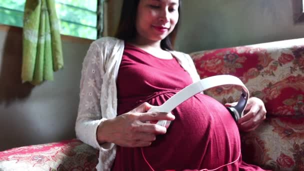 若いです妊娠中の女性座っています上のソファリスニング音楽 — ストック動画