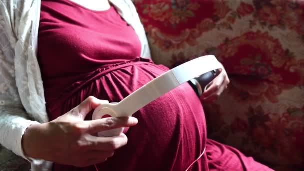 若いです妊娠中の女性座っています上のソファリスニング音楽 — ストック動画
