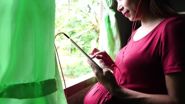 Mulher Grávida Jovem Perto Janela Usando Tablet Digital Ouvir Música — Vídeo de Stock