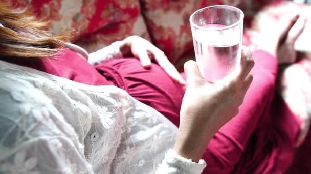 年轻的孕妇坐在沙发上喝水 — 图库视频影像
