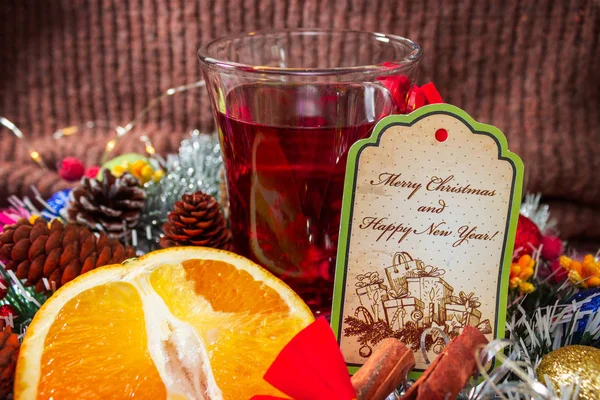 Mug of hot mulled wine sliced citrus and cinnamon stick. Gift envelope on New Year decorations background. Christmas concept