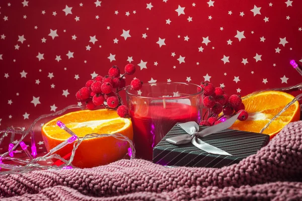 Noel konsepti. Bokeh tatil ışıkları. Yeni yıl kartı. Sulu portakallar, hediye kutusu dekoratif elma, kırmızı böğürtlen ve kalın süveter ve yıldızlı kırmızı arka plan.