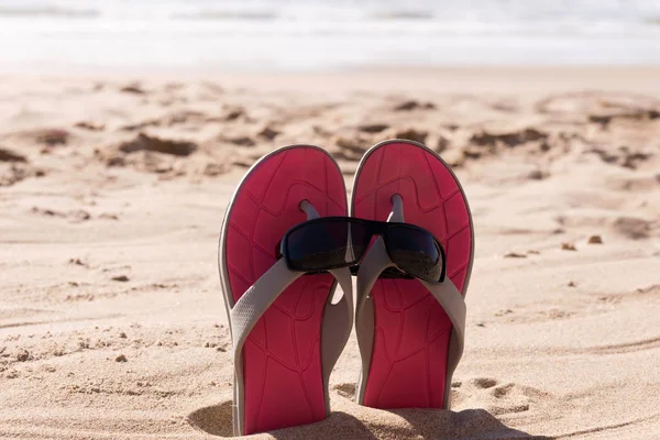 Par chinelos com óculos de sol na areia da praia — Fotografia de Stock