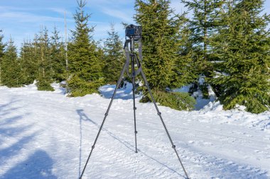 Tripod üzerinde kamera üzerinde orman yolu kışın duruyor.