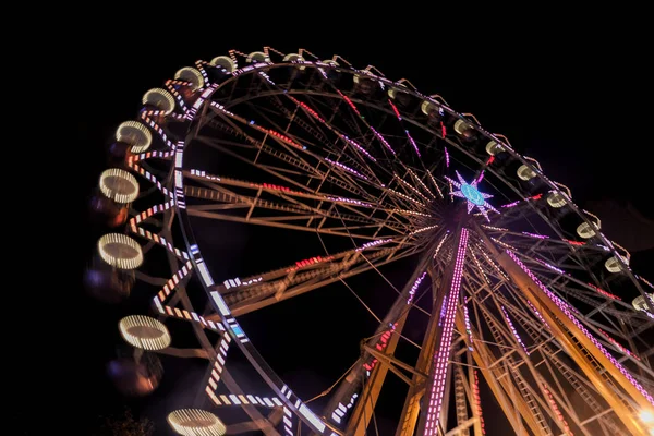 Rueda de la fortuna en la noche con un desenfoque de movimiento y bengalas de lentes — Foto de Stock