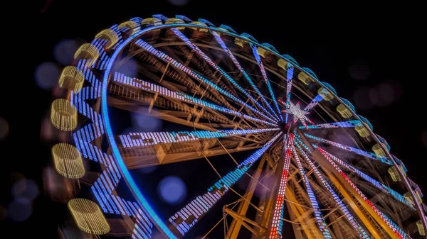 Rueda de la fortuna en la noche con un desenfoque de movimiento y bengalas de lentes — Foto de Stock