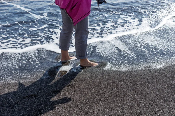 Mulher com os pés nus na água na praia preta — Fotografia de Stock