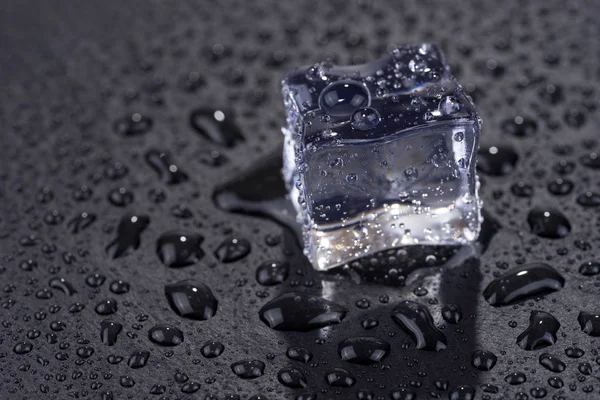 Single ice cube with water drops isolated on black background