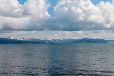 Deniz ve ağır beyaz bulutlar dağlarla çevrili ve parlak bir günde çekilen su üzerindeki güzel yansımalarla çevrili.