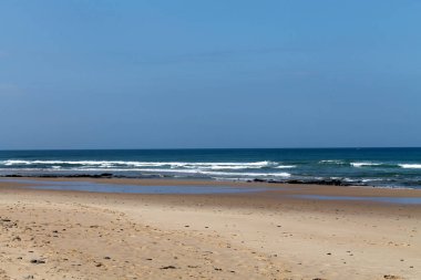 Dalgalar, sahil, okyanus ve mavi gökyüzü güneşli bir günde çekiliyor. Rahatlamak için seyahat cenneti.  