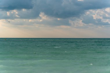 Deniz manzarası ve fırtınalı gökyüzü, gri bulutlar. Yağmur yağmaya başlamak üzere. Güneş yok, etrafta insanlar var.. 